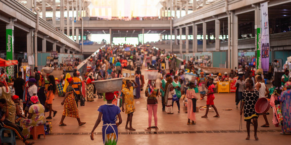 There is a market in the global south. There are people walking around with goods on their heads, balancing them