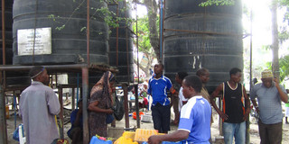 Leute mit Wassercontainern, die Trinkwasser aus einem riesigen Wassertank abfüllen möchten